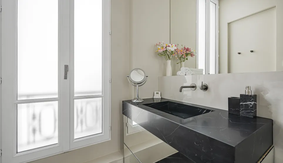 Luxury bathroom featuring black marble vanity and modern design. Elegant, refined ambiance with a bright window.