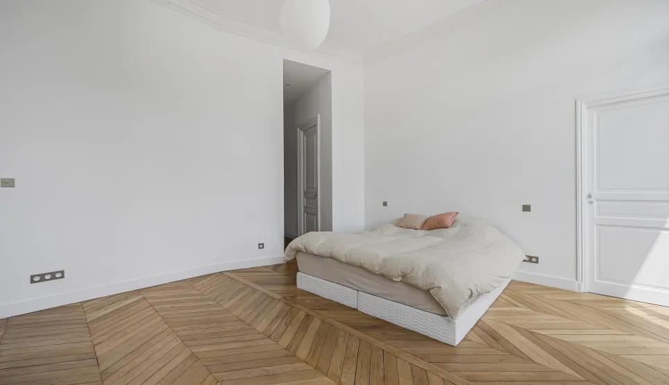 Luxury minimalist bedroom, chevron parquet, white walls. Parisian elegance, natural light. Ideal Haussmannian apartment.