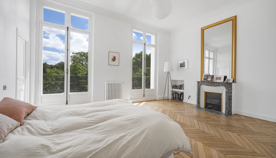 Luxurious bright bedroom with stunning green views. Herringbone parquet, fireplace and gilded mirror. Elegance and comfort.