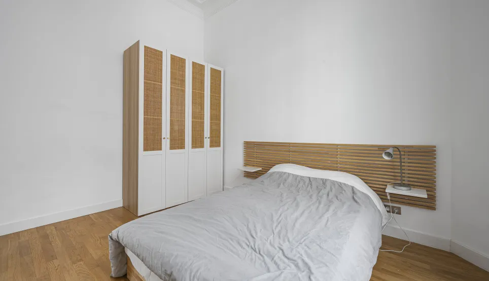 Modern, bright bedroom featuring wood flooring, designer slatted headboard, and elegant rattan wardrobe. Perfect for luxury apartment.