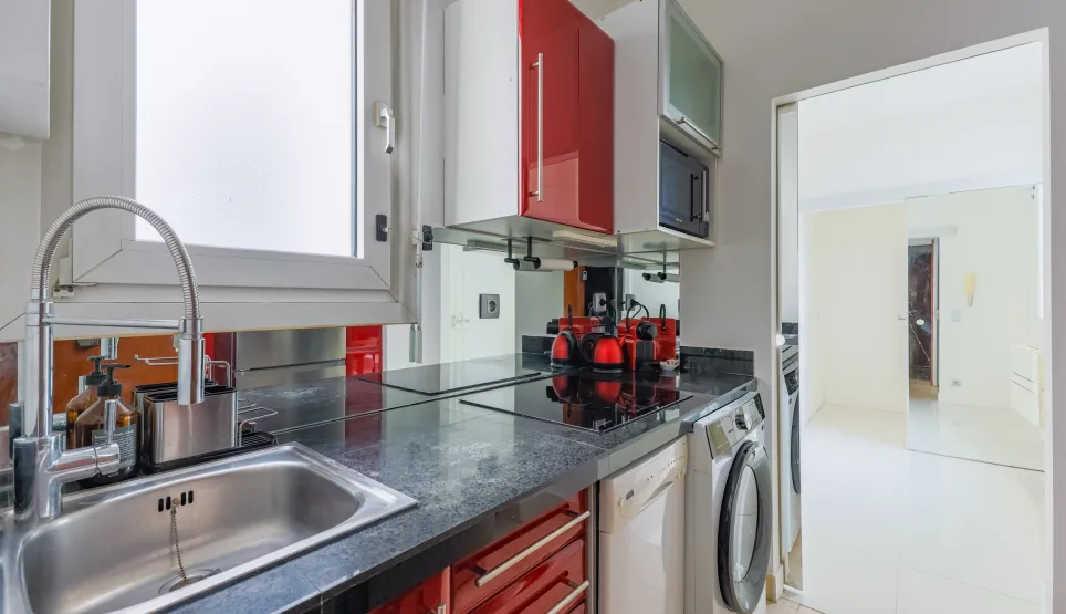 Sleek compact kitchen with red gloss cabinets, black granite, integrated appliances. Perfect for modern urban apartments.