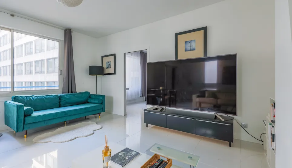 Bright, modern living room featuring a teal velvet sofa, large TV, and sleek design. Perfect for a luxury urban apartment. Comfort and style.