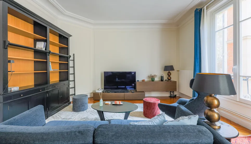 Elegant Parisian luxury living room with built-in bookshelf, designer sofa & TV. Bright and modern apartment space.