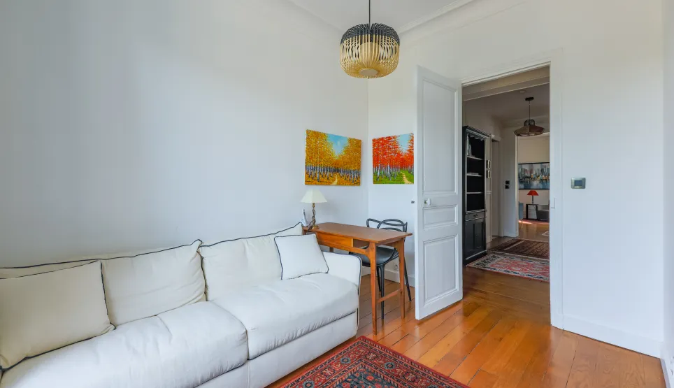 Bright, refined living space: designer sofa, elegant desk, warm hardwood floors, vibrant art. Ideal for a prestigious interior.