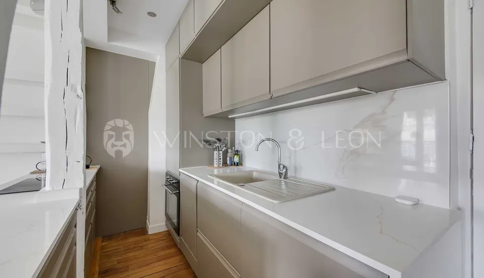 Modern, elegant kitchen with light grey cabinets, marble countertop & backsplash. Luxurious design for Parisian apartment.