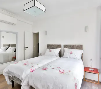Elegant modern bedroom with twin beds, air conditioning, mirror, and floral decor. Comfort and design for your luxury property.