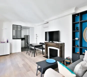 Bright modern living room with open kitchen, fireplace, and vibrant blue built-in shelving. Luxury apartment design.