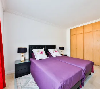 Elegant bedroom with twin beds, purple bedding, designer nightstands, and built-in wardrobes. Comfort and style for luxury property.