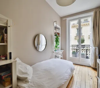 Bright Parisian bedroom with balcony, hardwood floor & city view. Single bed, built-in storage. Ideal for a child or extra office space. Charm & potential.