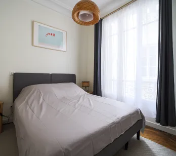 Elegant, bright bedroom with double bed, modern decor, and large window providing beautiful natural light. Perfect for a luxury apartment.