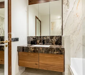 Modern luxury bathroom. Light and dark veined marble, elegant wooden vanity, and large mirror. High-end interior design.