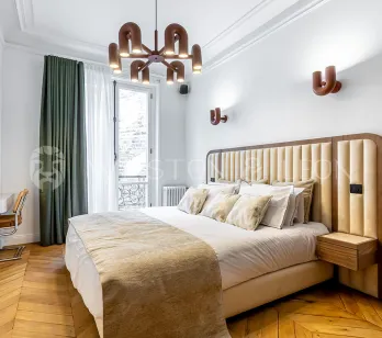 Modern luxury bedroom featuring a padded headboard, herringbone parquet, designer lighting, and balcony. Parisian elegance and comfort redefined.