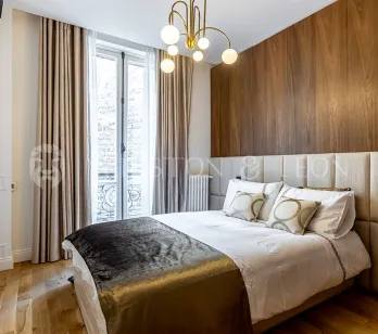 Modern luxury bedroom featuring wood paneling, padded headboard, and elegant chandelier. Contemporary design and comfort for a Parisian apartment.