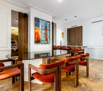 Modern luxury interior: elegant dining room with glass table, orange velvet chairs, contemporary art, and parquet. Refined design.