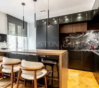 Modern luxury kitchen with wood island, veined black marble, designer stools & pendant lights.