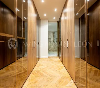 Modern luxury dressing room with wood and glass cabinets, herringbone parquet. Elegant storage for high-end property.