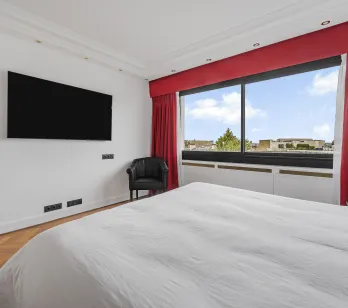 Bright, modern master suite with city views, TV, armchair, and hardwood floor. The luxury and comfort of a high-end apartment.