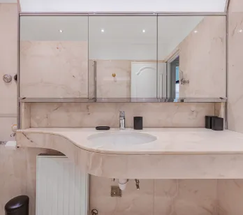 Luxurious light marble bathroom, designer sink and mirror. Refined ambiance for an exceptional property.