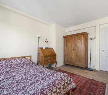 Elegant bedroom with antique solid wood furniture: wardrobe, secretary desk. Comfortable bed, hardwood floor, oriental rug. Timeless charm.