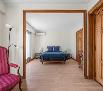 Bright, elegant master suite with blue double bed, light hardwood floors & refined furnishings. A charming luxury property interior.
