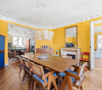 Elegant Parisian dining room with yellow walls, herringbone parquet, fireplace. Renovated luxury apartment, blending old charm & modern design.
