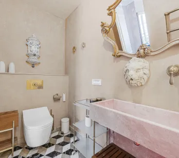 Luxury bathroom with pink marble sink, gold mirror, designer toilet and geometric tiles. Elegant and refined ambiance.