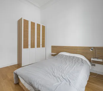 Modern, bright bedroom featuring wood flooring, designer slatted headboard, and elegant rattan wardrobe. Perfect for luxury apartment.