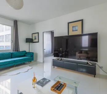 Bright, modern living room featuring a teal velvet sofa, large TV, and sleek design. Perfect for a luxury urban apartment. Comfort and style.