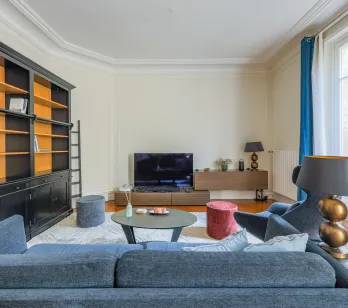 Elegant Parisian luxury living room with built-in bookshelf, designer sofa & TV. Bright and modern apartment space.