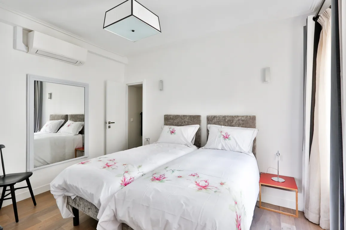 Elegant modern bedroom with twin beds, air conditioning, mirror, and floral decor. Comfort and design for your luxury property.
