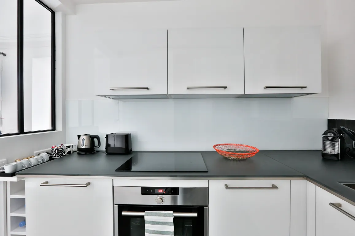 Sleek white modern kitchen with integrated appliances, dark countertop. Perfect for luxury apartment living.