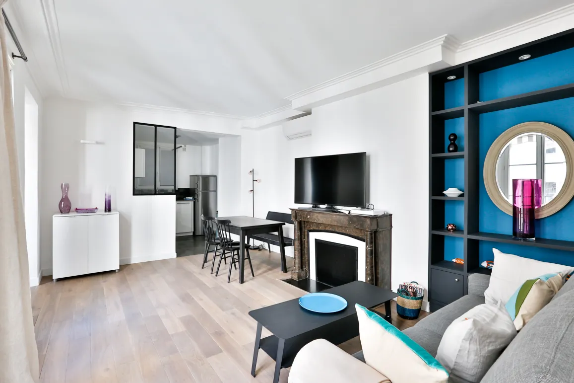 Bright modern living room with open kitchen, fireplace, and vibrant blue built-in shelving. Luxury apartment design.