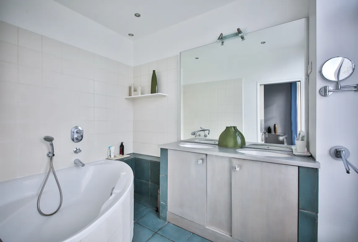 Modern luxury bathroom: bathtub, double vanity, large mirror, white/blue tiles. Sleek design, serene ambiance. Perfect for high-end property.
