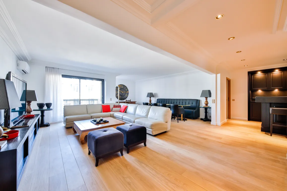 Spacious, bright luxury living room with light wood floors, modern sectional sofa, dining area, and integrated bar. High-end contemporary design.
