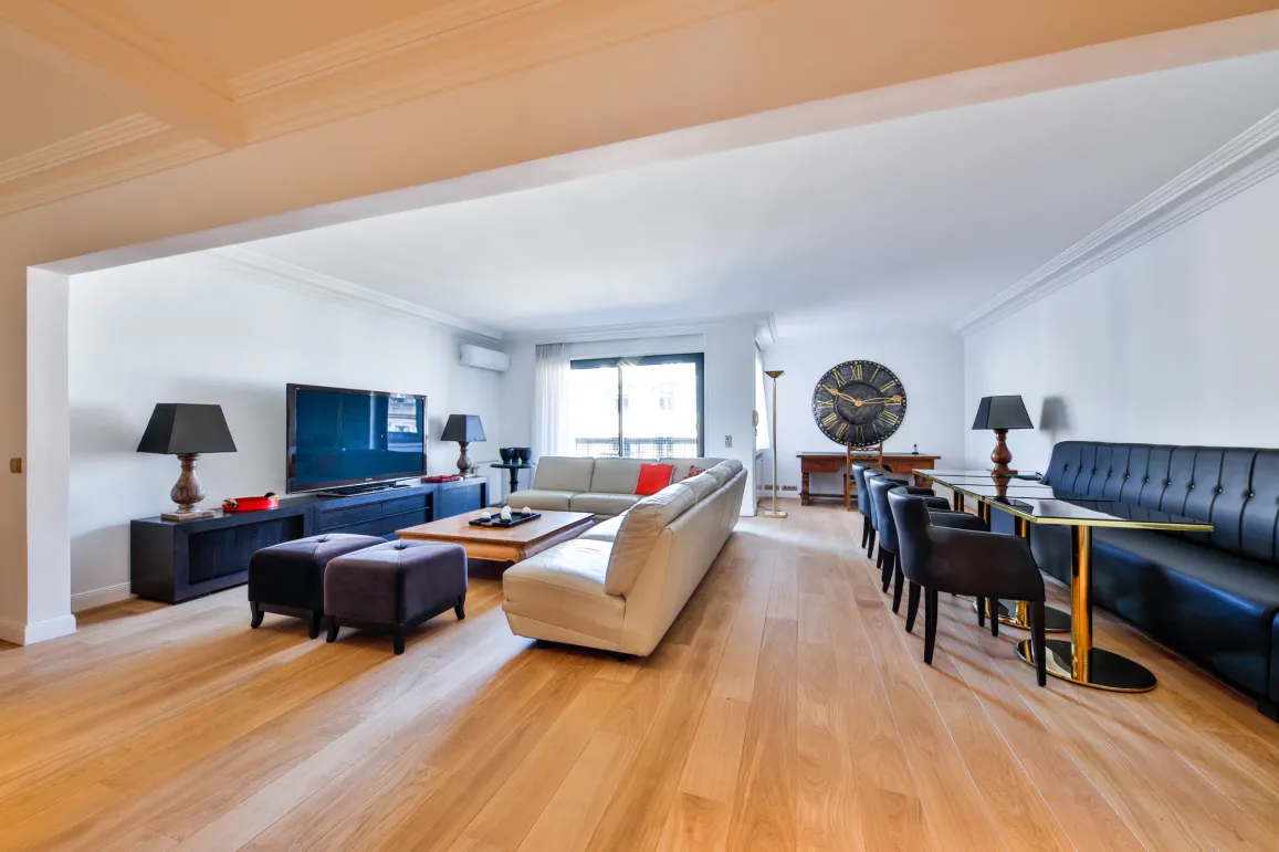 Spacious, modern living and dining room with light wood floors, designer furniture, and large TV. Perfect for a luxury apartment.