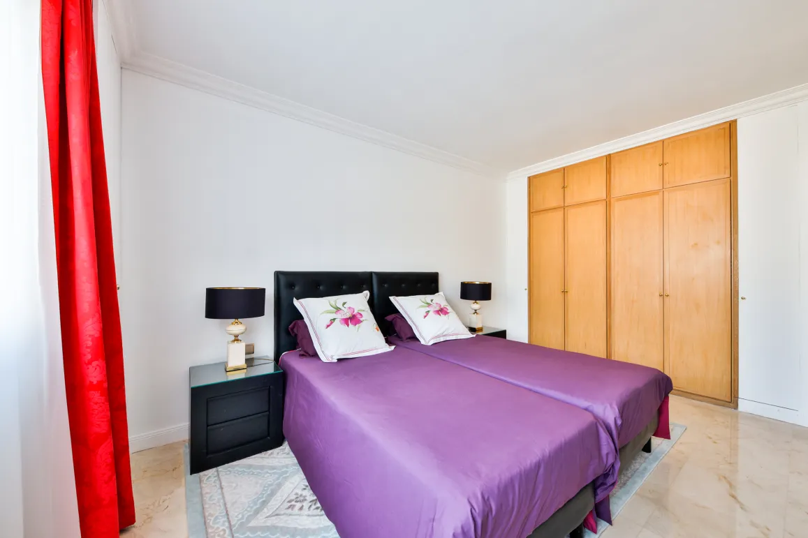 Elegant bedroom with twin beds, purple bedding, designer nightstands, and built-in wardrobes. Comfort and style for luxury property.