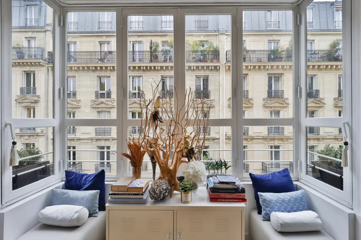 Luxury apartment with stunning Paris view. Panoramic window, elegant reading nook, refined interior design. Abundant natural light.