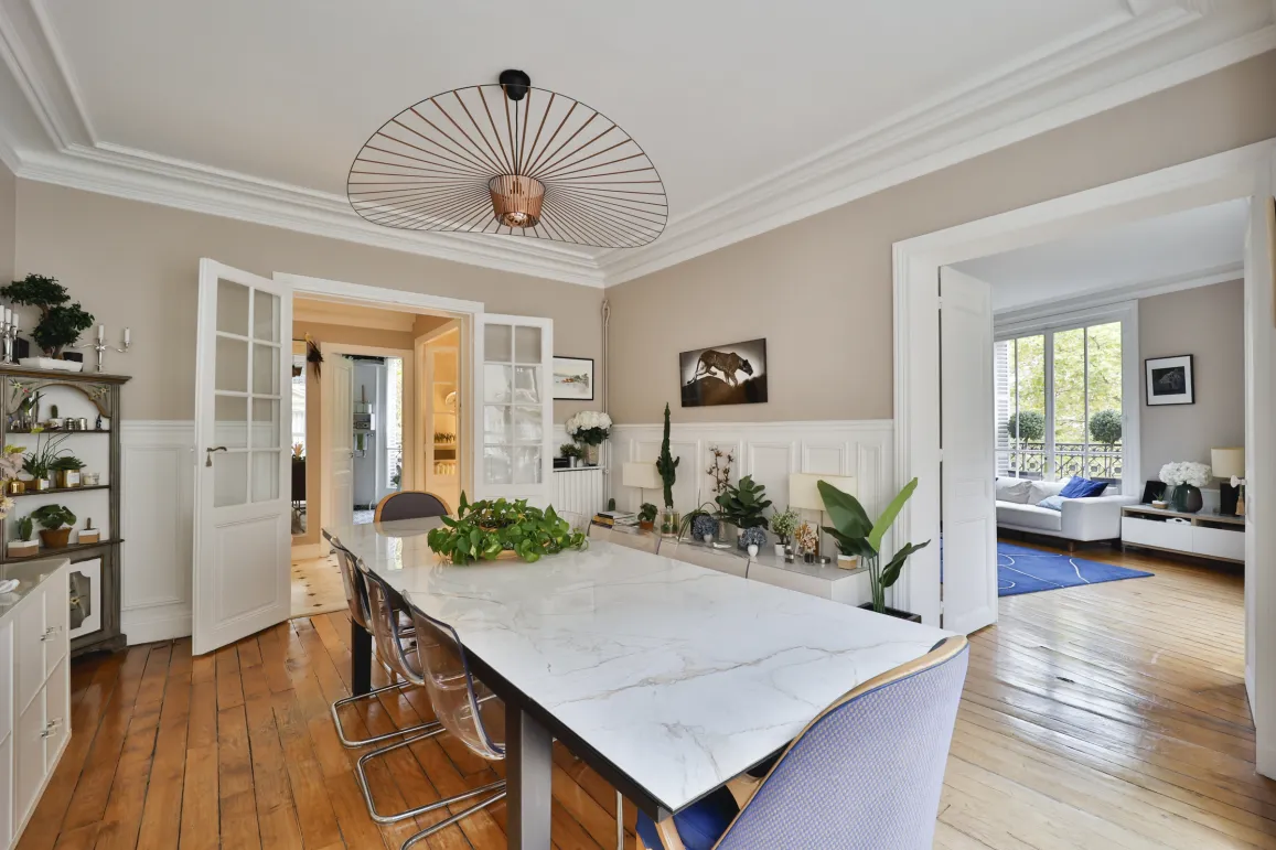 Stunning luxury dining room featuring marble table, designer chandelier, hardwood floors & moldings. Open space leading to a bright living room. Modern elegance.