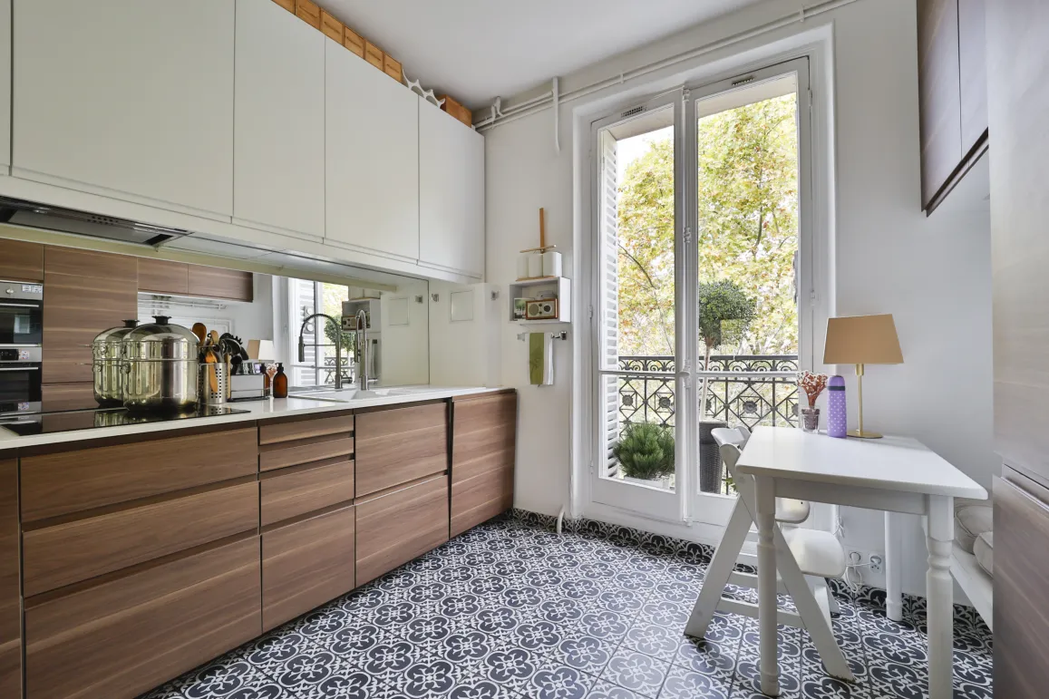 Modern luxury kitchen: wood cabinets, patterned tiles, balcony with tree view. Parisian chic apartment.