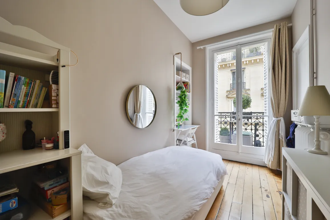 Bright Parisian bedroom with balcony, hardwood floor & city view. Single bed, built-in storage. Ideal for a child or extra office space. Charm & potential.