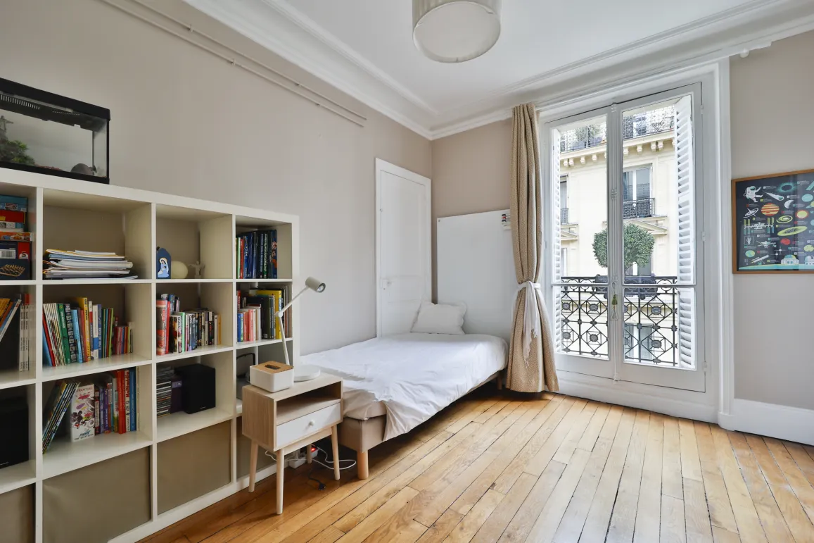 Bright bedroom with hardwood floors, French window, and balcony. Minimalist design, optimized space. Perfect for a luxury Parisian studio.