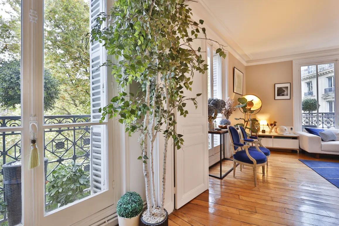 Bright luxury living room with balcony, hardwood floor & green view. Chic Parisian ambiance, elegant furniture. High-end apartment.
