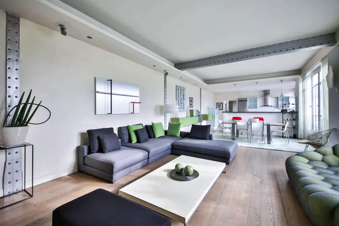 Luxury open-plan living-kitchen. Contemporary design, modular grey-green sofa, industrial beams. Bright modern ambiance for chic apartment.