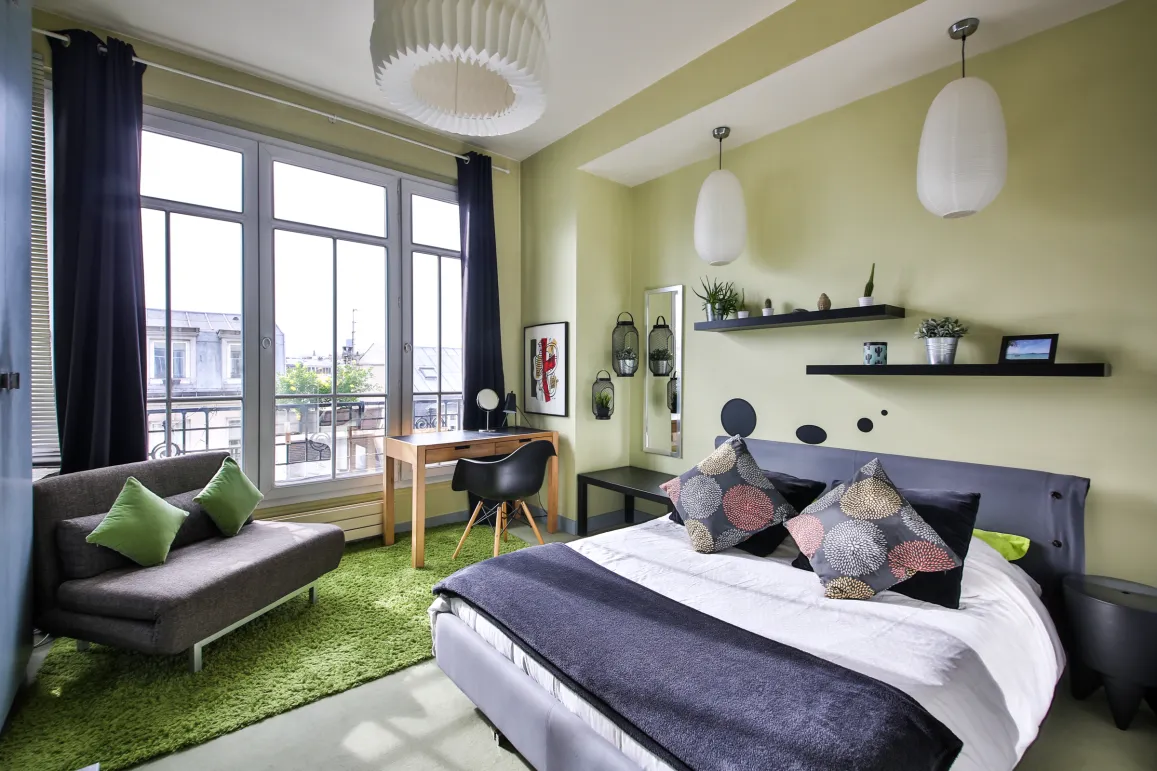 Bright modern bedroom with city view, contemporary design, comfortable bed, desk area, and lounge corner. Perfect luxury apartment.