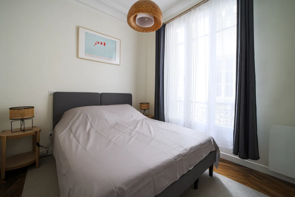 Elegant, bright bedroom with double bed, modern decor, and large window providing beautiful natural light. Perfect for a luxury apartment.