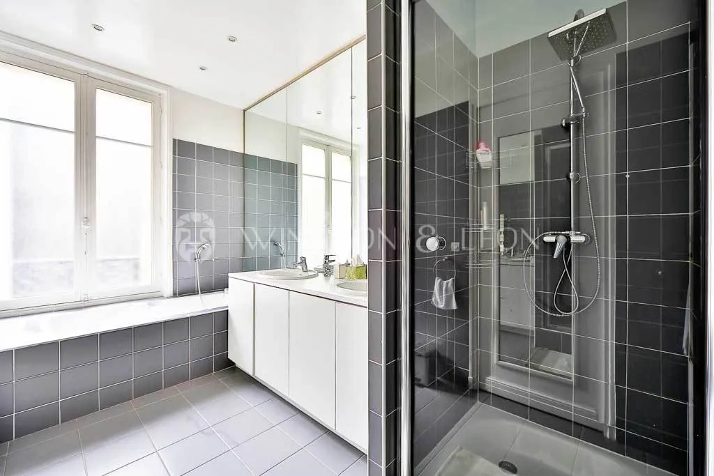 Bright, modern bathroom featuring double vanity, bathtub, and walk-in shower. Contemporary design with elegant grey tiling.