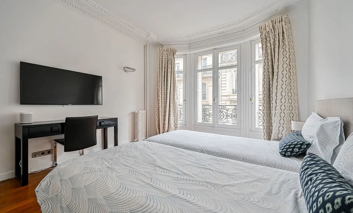Luxury Parisian twin bedroom, desk, TV, large window, classic moldings. City view. Elegant and modern comfort.