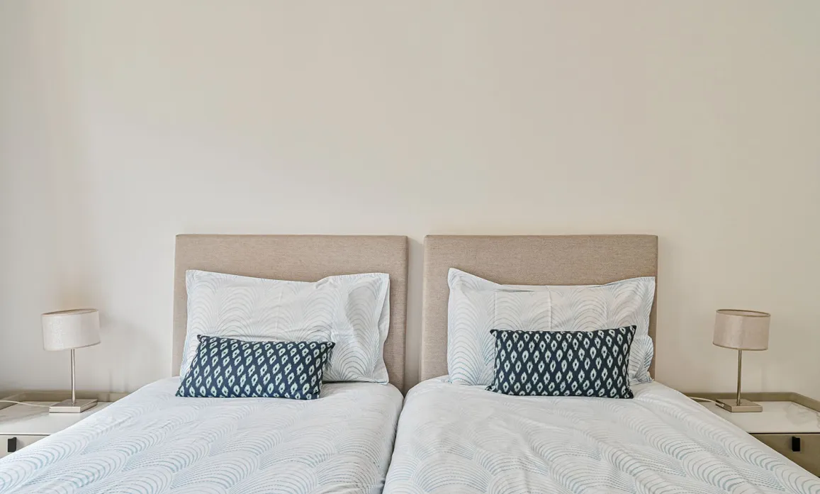 Luxury twin bedroom with elegant beige headboards, crisp white bedding, and blue accent pillows. Modern design, serene ambiance for a refined stay.