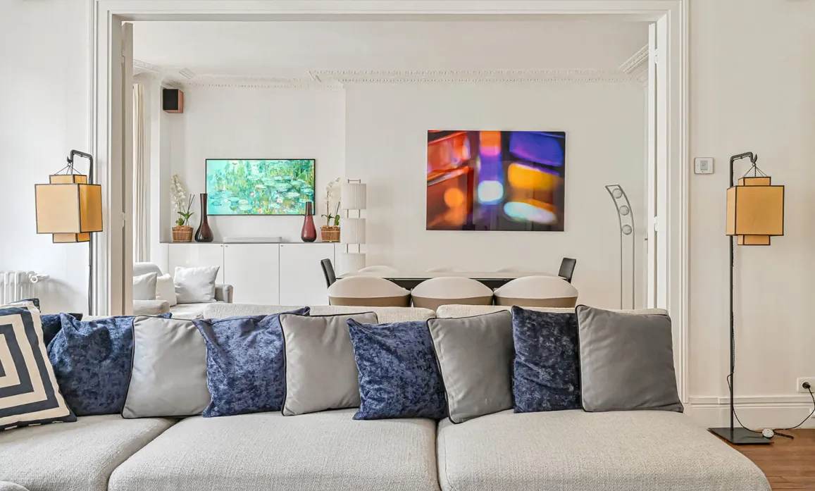 Modern luxury living room featuring a grey sectional sofa, blue cushions, and contemporary abstract art. Elegant interior design with a refined ambiance.