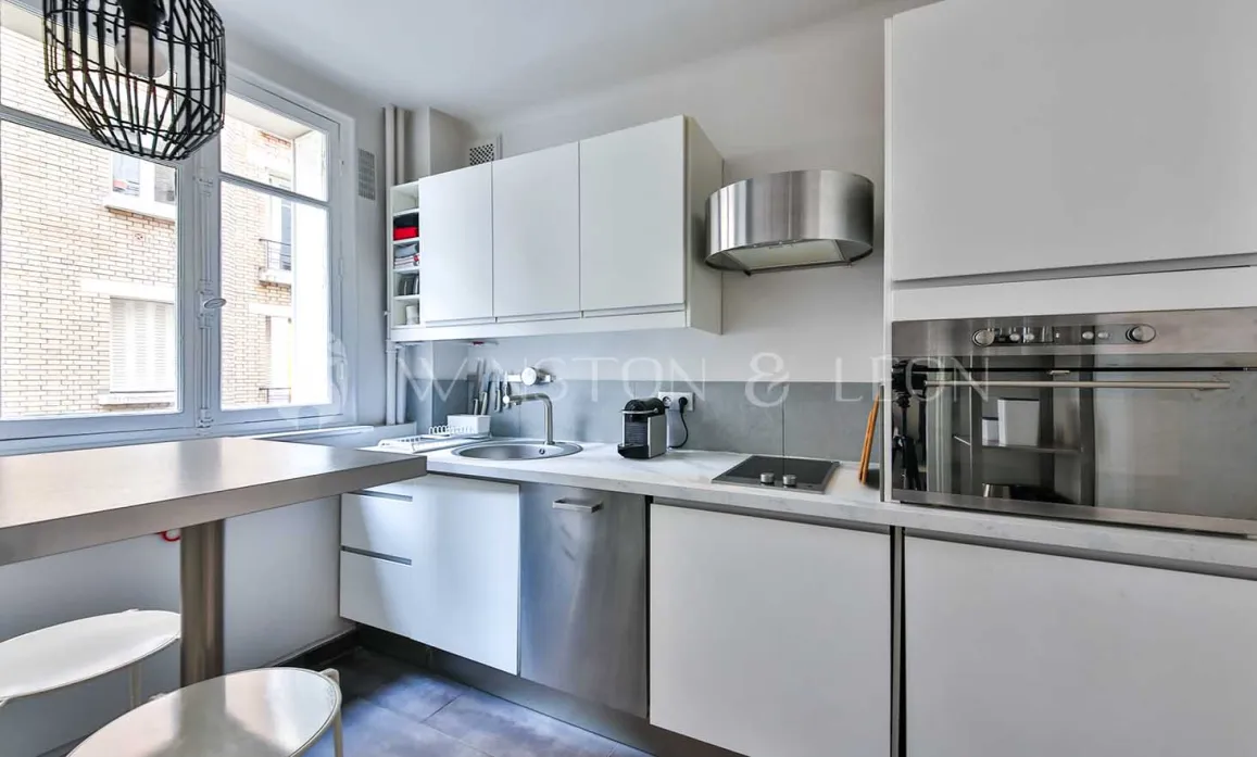 Bright modern kitchen, sleek white cabinetry, integrated stainless steel appliances, dining area. Contemporary design ideal for luxury apartment.